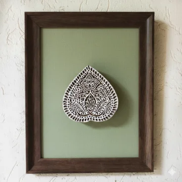 Bloc de bois sculpté indien en forme de goutte exposé dans un cadre en bois sombre sur fond textile vert